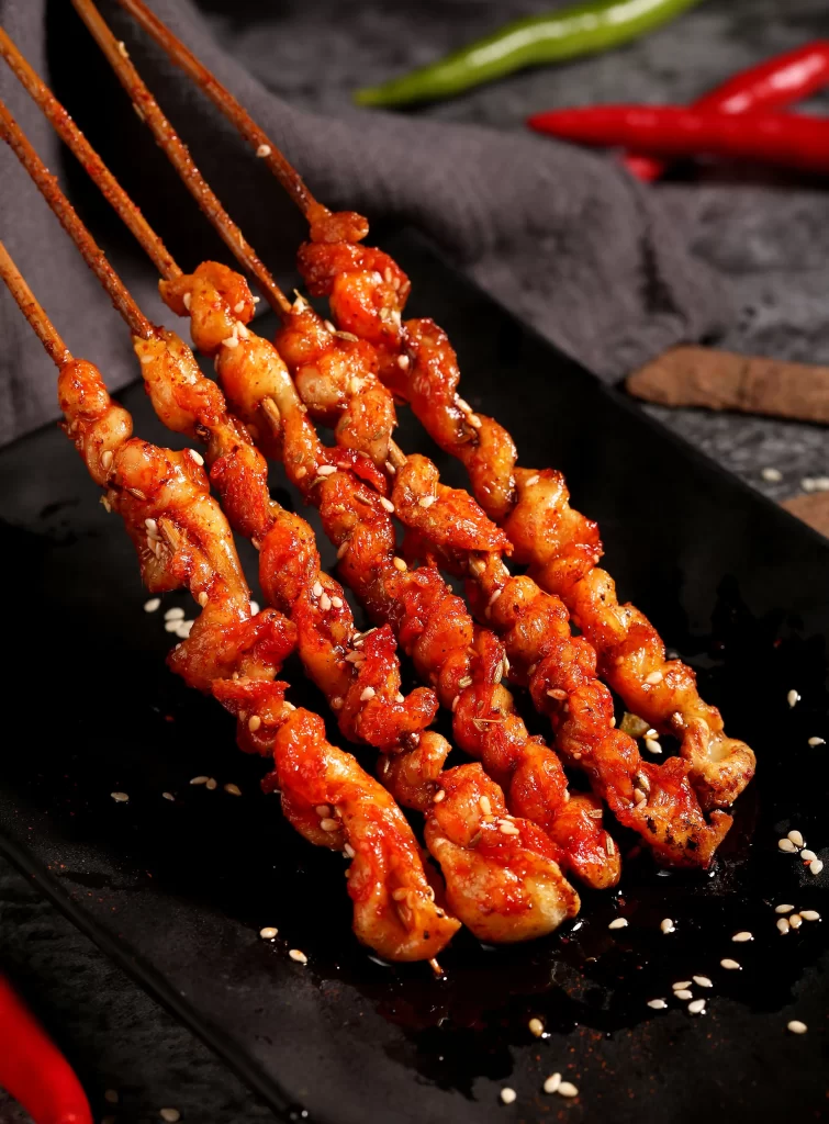 Spicy Chicken Skewers Red Sauce Sesame Garnish Black Plate