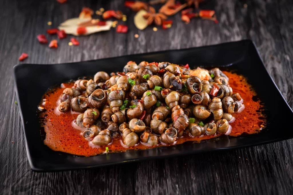 Spicy Grilled Snails Red Sauce Garnish Black Plate