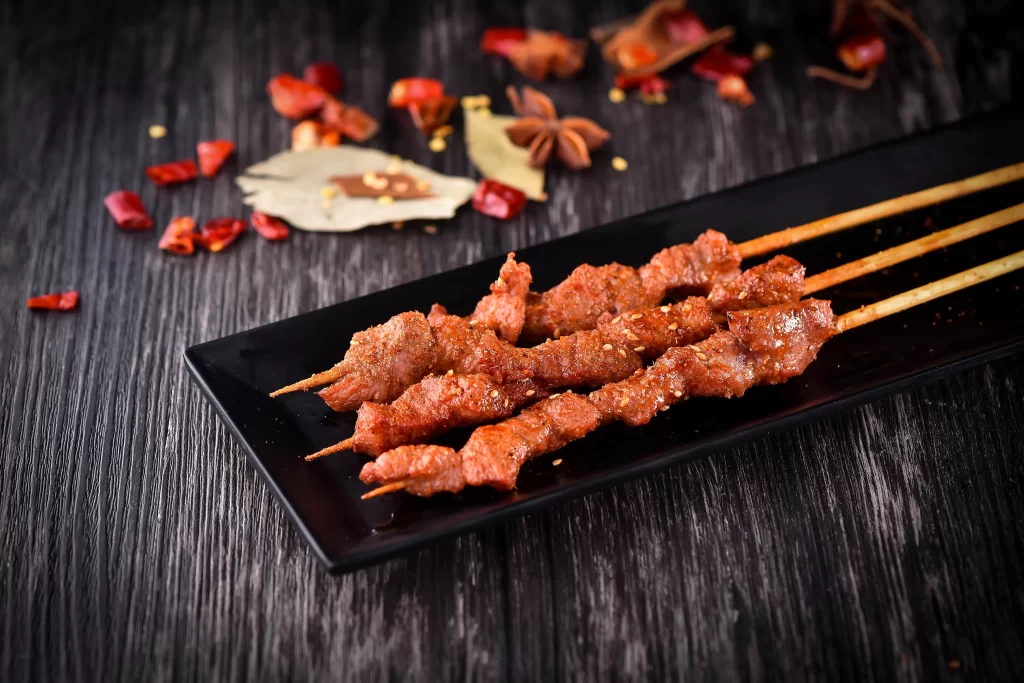Spicy Pork Skewers Charred Crust Sesame Garnish Black Plate