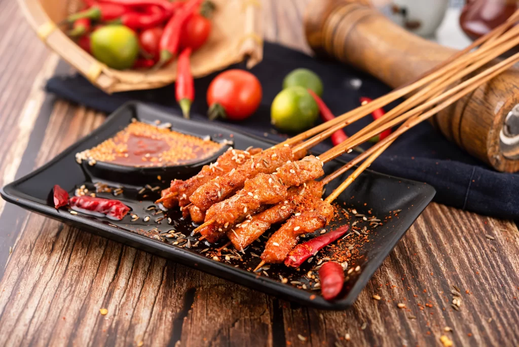 Spicy Pork Skewers Red Chili Sauce Sesame Garnish Black Plate