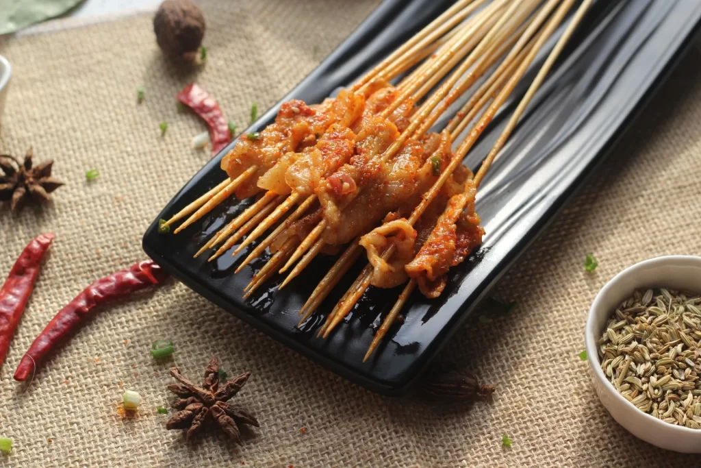 Spicy Pork Skewers Red Sauce Charred Edges Black Plate