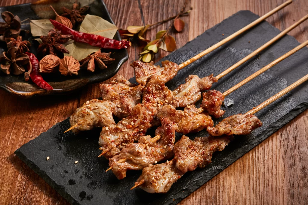 Spicy Pork Skewers Sesame Garnish Charred Edges Black Slate