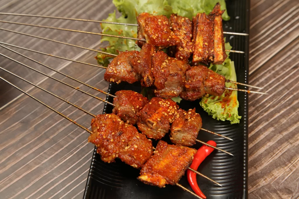 Spicy Pork Skewers Sesame Garnish Fresh Lettuce Black Plate