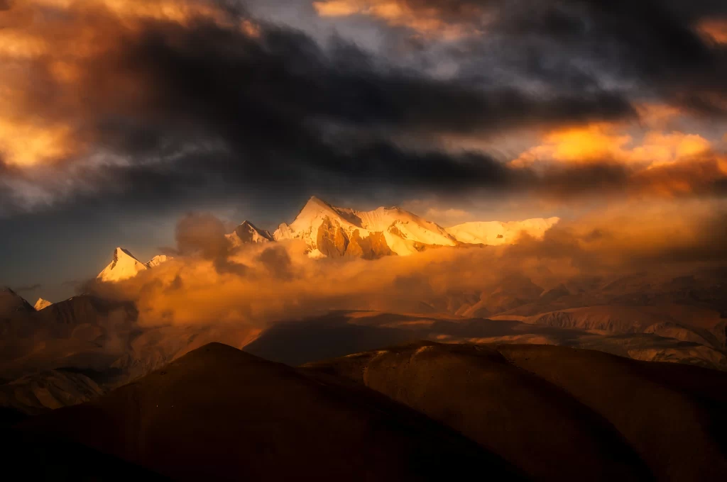 sunset golden-orange majestic snow-capped peaks dramatic clouds rugged terrain mountain