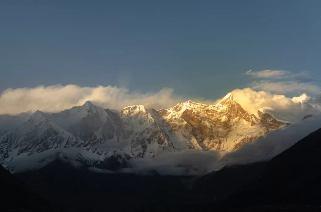 sunset golden snow-capped peaks deep blue sky fluffy clouds rugged