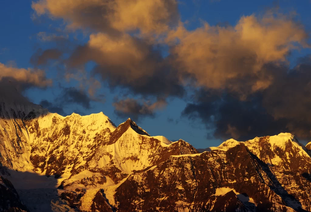 sunset golden snow-capped peaks dramatic clouds deep blue sky rugged