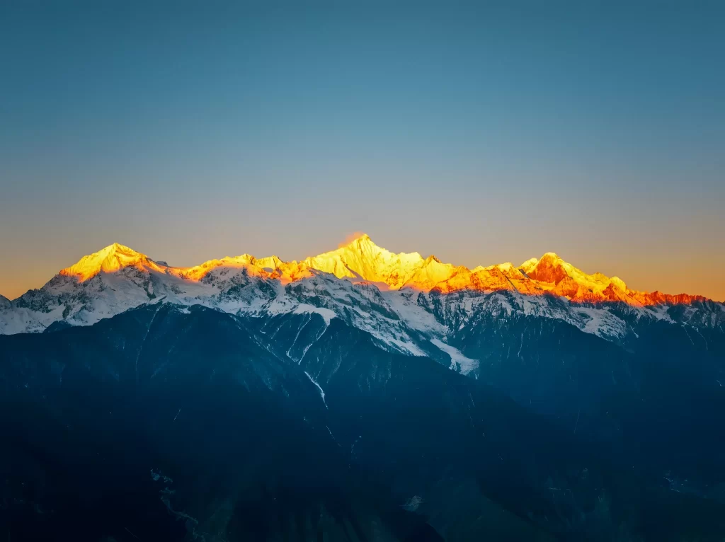 sunset golden snow-capped peaks deep blue sky rugged terrain mountain
