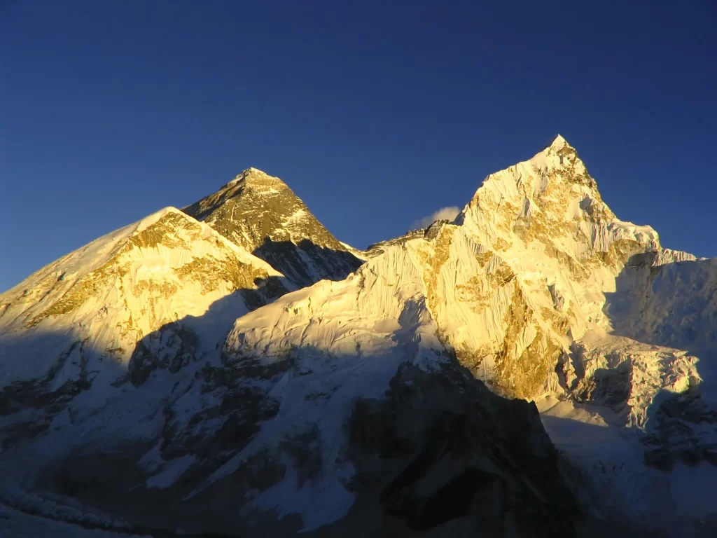 sunset golden snow-capped blue sky mountain peaks shadows rugged terrain