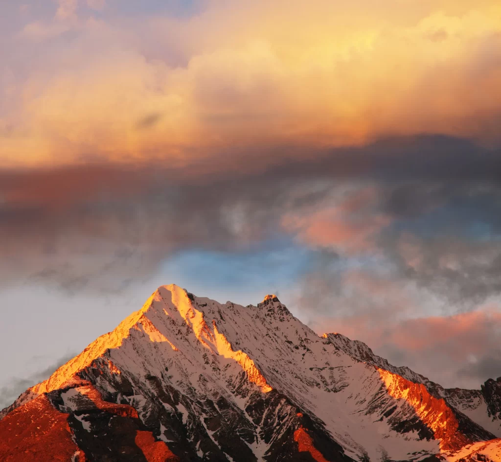 sunset golden snow-capped peaks dramatic clouds warm rugged terrain serene