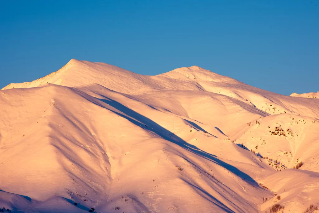 sunset golden snow-covered peaks clear blue sky long shadows rugged