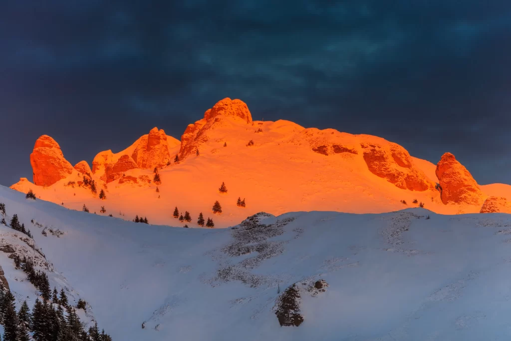 sunset golden snow-covered peaks deep blue sky rugged terrain evergreen
