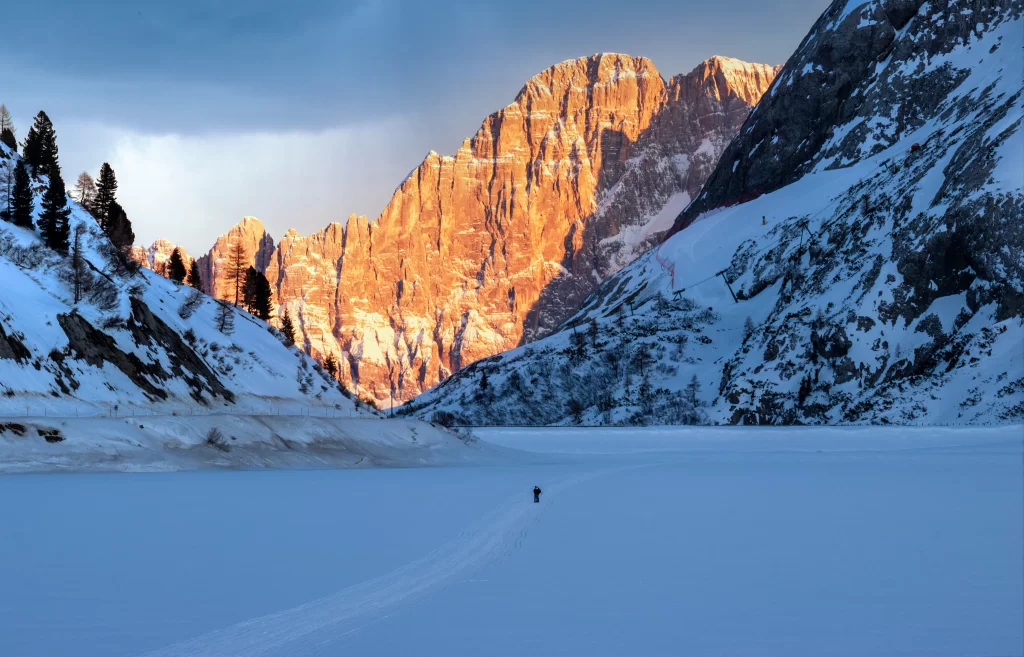 sunset golden snowy peaks rugged terrain tranquil lake solitary figure