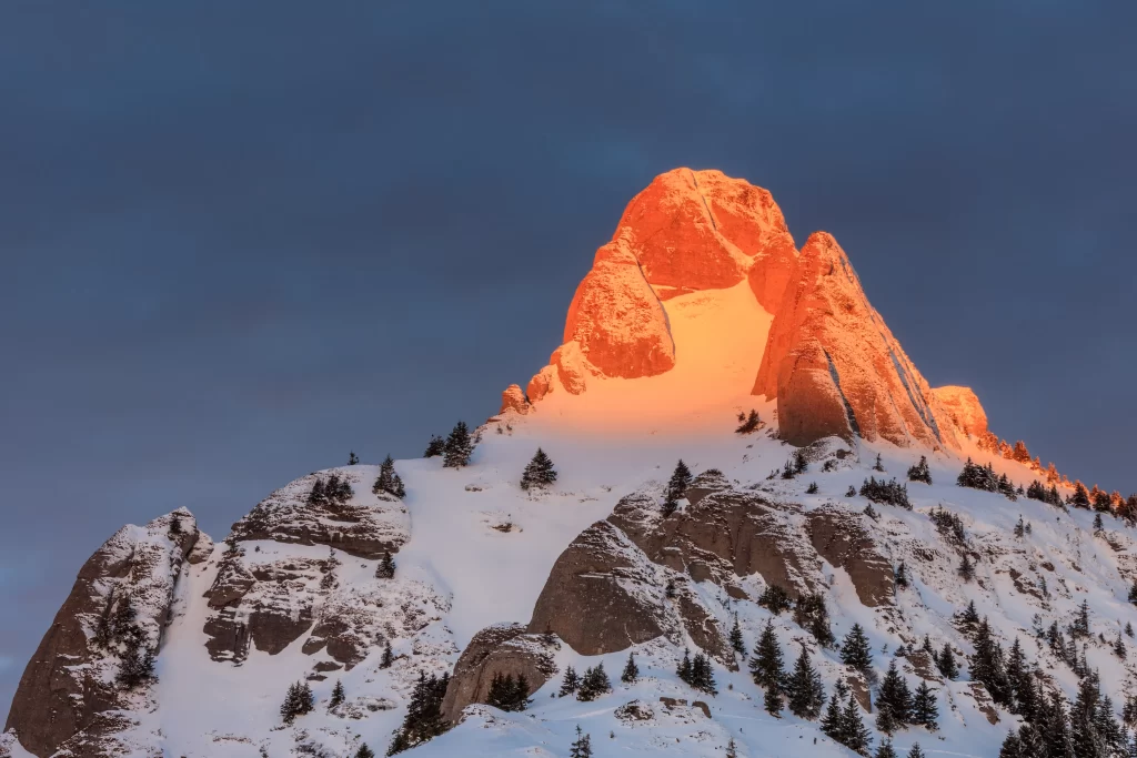 sunset snow-covered peaks orange clear sky rugged terrain pine trees