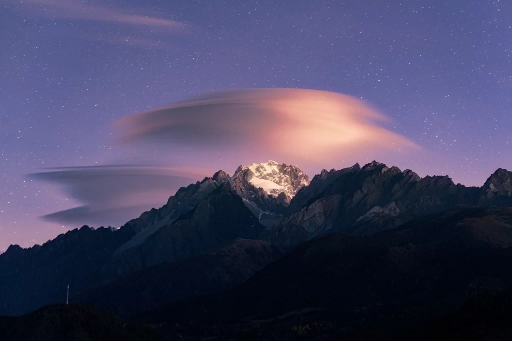 twilight starry sky golden clouds mountain peaks snow-capped rugged terrain
